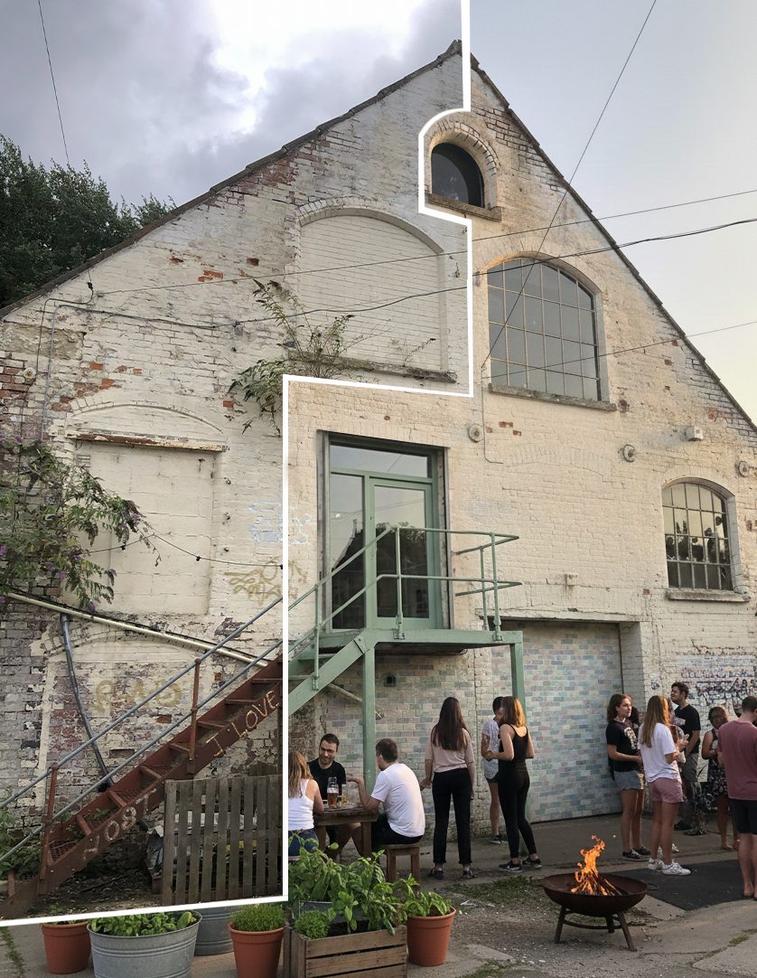 People gathered in the courtyard of a whitewashed former industrial building with an external stair