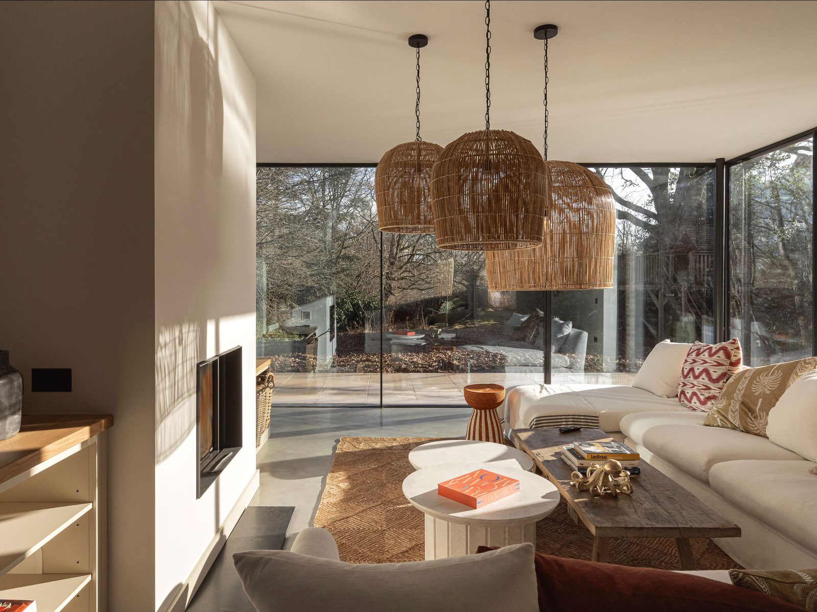 Living space with rattan pendant lights and full-height glazing looking out to woodland