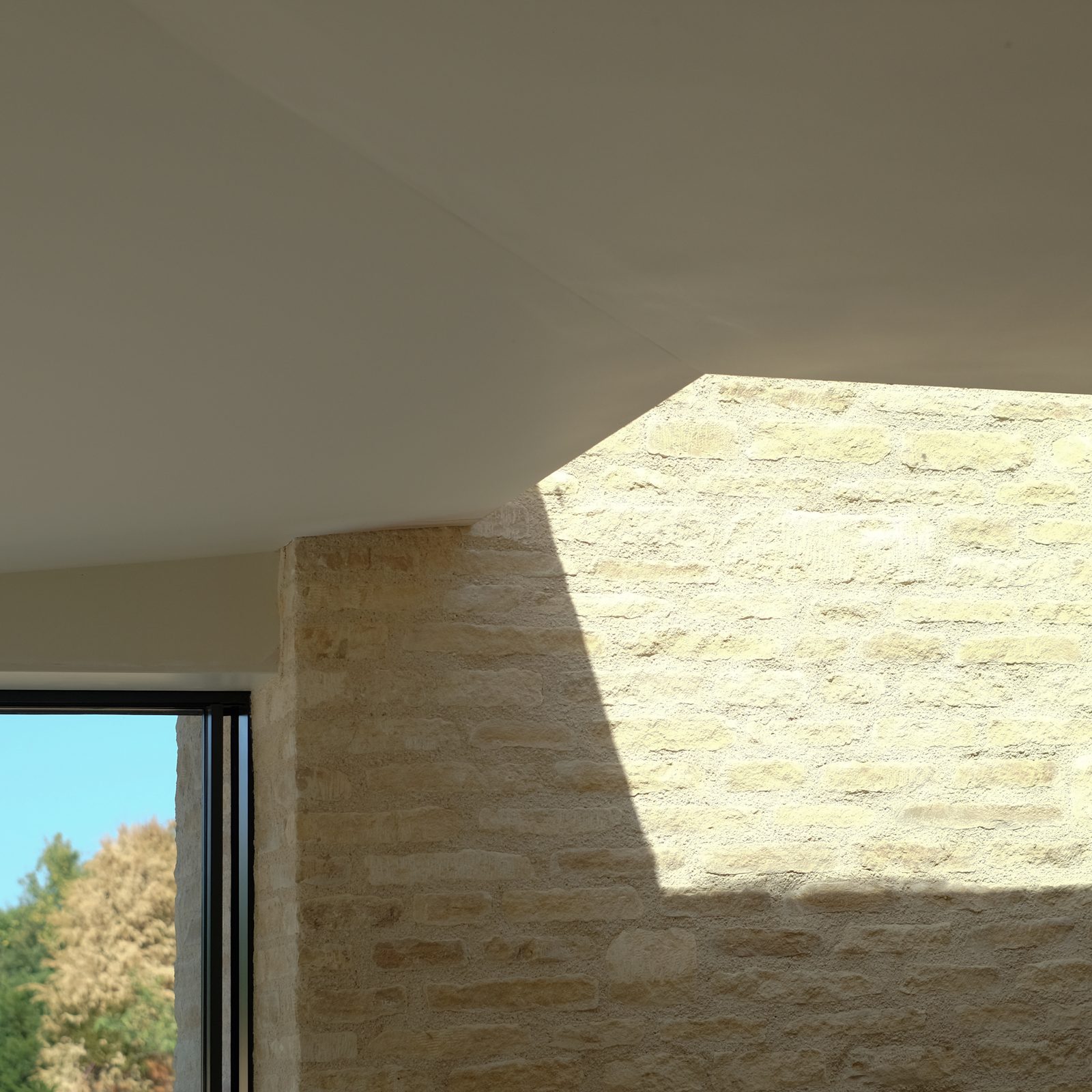 Inside the new extension, sunlight falling across the stone chimney breast beside a large window